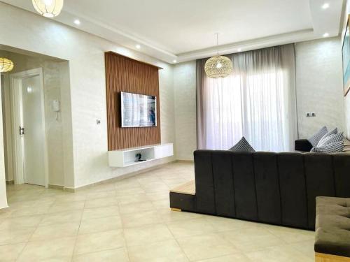 a living room with a black couch and a tv at Superbe Appartement avec Piscine - 5 min de la Plage à Imi Ouaddar in Imi Ouaddar