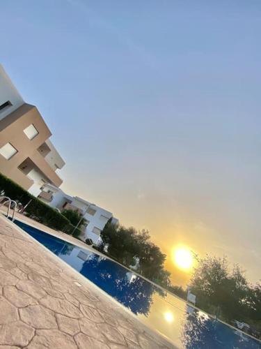 a view of a building and a swimming pool with the sunset at Superbe Appartement avec Piscine - 5 min de la Plage à Imi Ouaddar in Imi Ouaddar