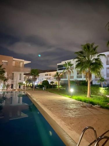 a swimming pool with palm trees and buildings at night at Superbe Appartement avec Piscine - 5 min de la Plage à Imi Ouaddar in Imi Ouaddar