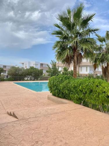a swimming pool with a palm tree and a building at Superbe Appartement avec Piscine - 5 min de la Plage à Imi Ouaddar in Imi Ouaddar