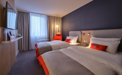 Holiday Inn Express München Messe, an IHG Hotel في فيلدكيرخن: غرفة فندقية بسريرين وكرسي احمر