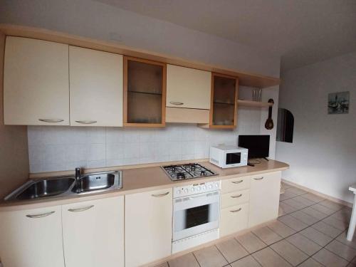 een keuken met witte kasten, een wastafel en een magnetron bij Apartment in Rosolina Mare 24985 in Rosolina Mare