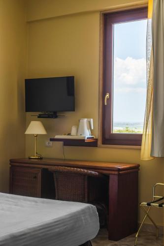 a bedroom with a desk with a television and a window at Apulia Hotel Taranto Ara Solis in Lido Azzurro