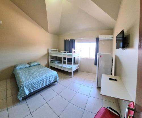 a small bedroom with a bed and a refrigerator at Pousada Girassol da Ferrugem in Garopaba