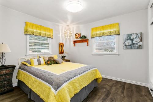 1 Schlafzimmer mit einem Bett mit gelber Bettwäsche und 2 Fenstern in der Unterkunft CUTE Remodeled Midcentury Cottage on Boise Bench in Boise