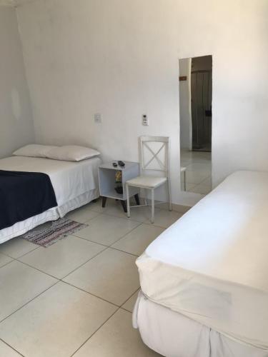a white room with two beds and a chair at Pousada Trilha do Sol in Pirenópolis