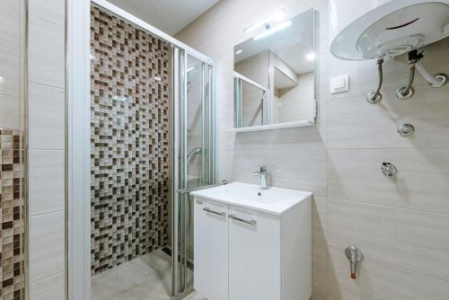 La salle de bains blanche est pourvue d'un lavabo et d'une douche. dans l'établissement Apartments Mrkan, à Cavtat