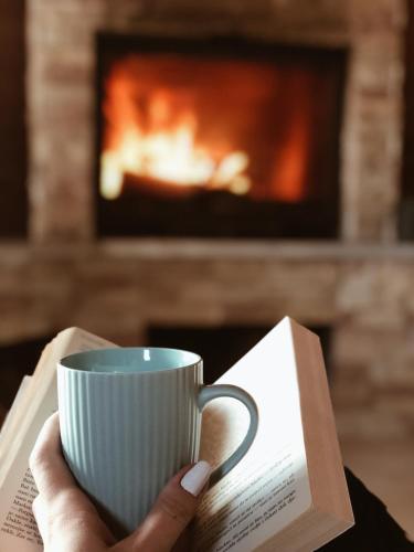 a person holding a cup of coffee and a book at Casa Mia Resort in Kupres