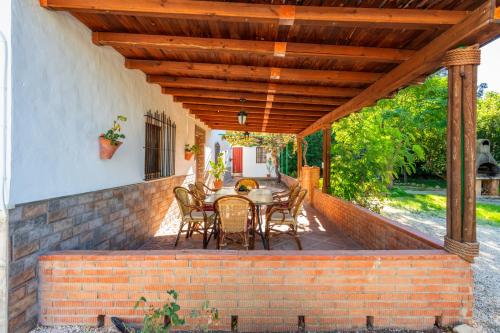 a patio with a table and chairs under a wooden roof at Casa La Encina in El Chorro