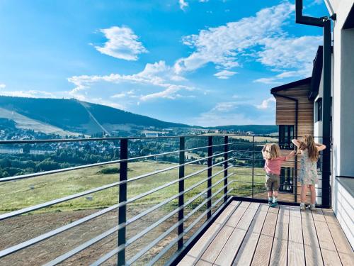 two little girls standing on a balcony looking out at the valley at Boutique apartment Heidi with mountain view in Loučná pod Klínovcem
