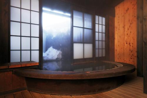 a bath tub in a room with windows at Okada Ryokan Warakutei in Takayama
