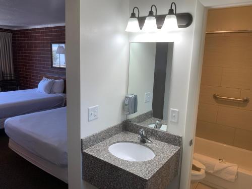 ein Bad mit einem Waschbecken, einem Bett und einem Spiegel in der Unterkunft Oquirrh Mountain Inn in Tooele