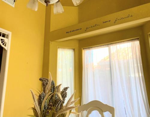 a dining room with yellow walls and two windows at Wildflower Haven room in Hemet