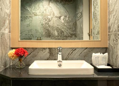 a bathroom sink with a mirror and a vase of flowers at Sann Hotel in Chiang Rai