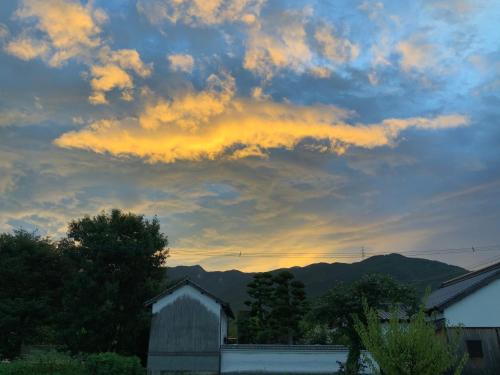 a cloudy sky at sunset with a barn and trees at Akitsuki Kominka Yado You in Asakura