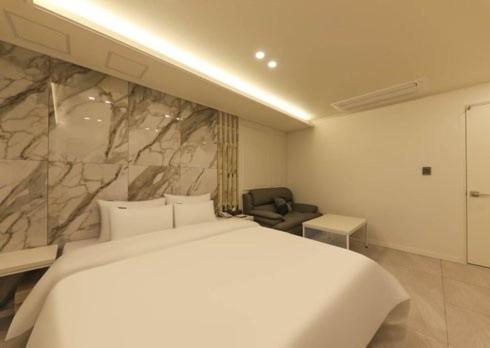 a bedroom with a white bed and a stone wall at Gwangju Brown Dot Chungjang in Gwangju