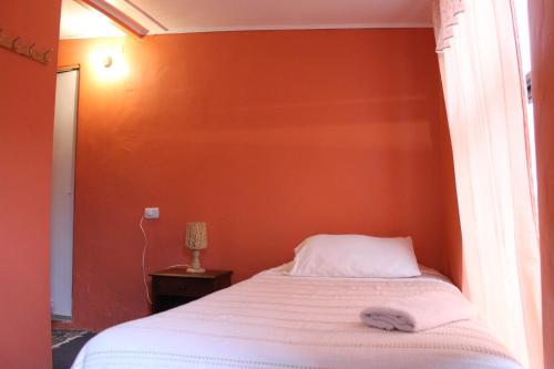 Cama en habitación con pared de color naranja en Hostal Cali, en Putre