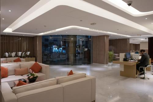 a lobby with white couches and a man working at a desk at Corp Executive Hotel Doha Suites in Doha