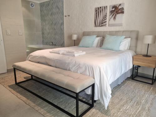 a large white bed with a bench in a bedroom at Beautiful apartment across from the beach in Cape Town