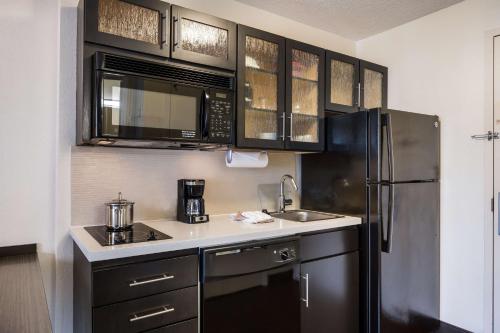 a kitchen with black cabinets and a stainless steel refrigerator at Sonesta Simply Suites Silicon Valley Santa Clara in Santa Clara
