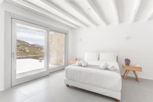 Dormitorio blanco con cama y ventana grande en Villa Salty, The above Alemagou experience, en Ftelia