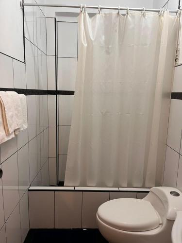 a bathroom with a white shower curtain and a toilet at Hotel Munay in Paracas