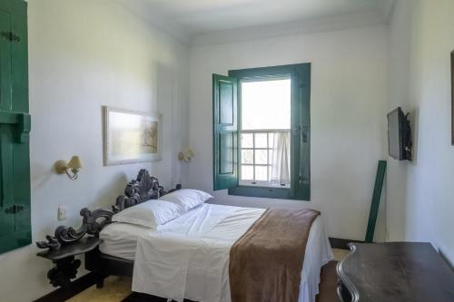a bedroom with a bed with white sheets and a window at Sítio Paraíso Beach Tennis in Vassouras