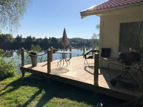 una terraza de madera con mesa y sombrilla en Cottage by the river en Avesta