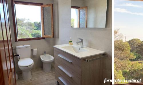 een badkamer met een wastafel, een toilet en een spiegel bij Apto Mar de Es Caló, a metros de la playa - Formentera Natural in Es Calo