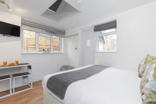 a white bedroom with a bed and two windows at Modern Self Contained Studio Home in Cheltenham