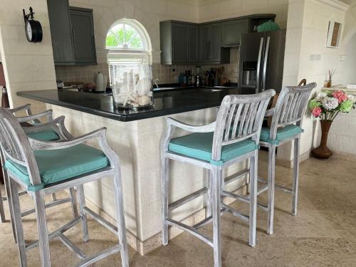 a kitchen with a counter with four bar stools at Barbados Luxury Villa with Pool in Saint James