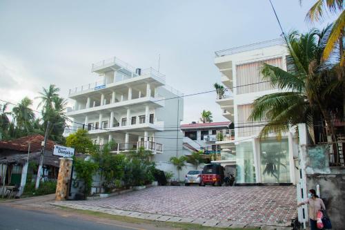 a white building on a street with palm trees at Resort Deepika Mirissa in Mirissa