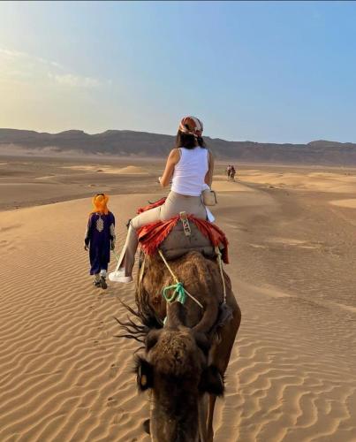 a woman riding on the back of a camel in the desert at Bivouac ZAGORA in Zagora