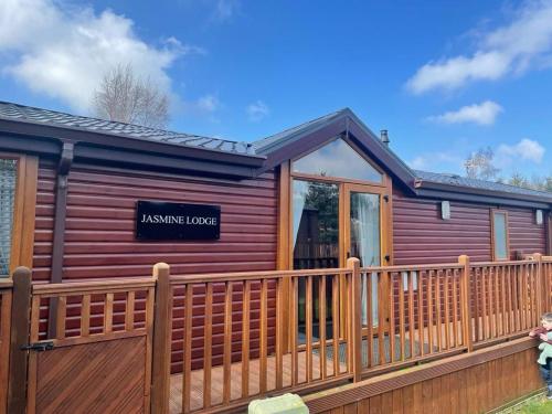 a log cabin with a wooden fence at Jasmine Lodge, 2 bedroom with hot tub - Felmoor Park in Felton