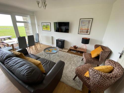 una sala de estar con un sofá de cuero negro y sillas en SEAVIEW self-catering coastal bungalow in rural West Wight en Freshwater