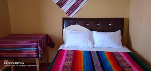 1 cama con manta multicolor y almohadas blancas en Paqariy lodge, en Ocosuyo