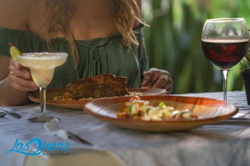 a woman sitting at a table with a plate of food and wine at Las Dunas Surf Resort in Aposentillo