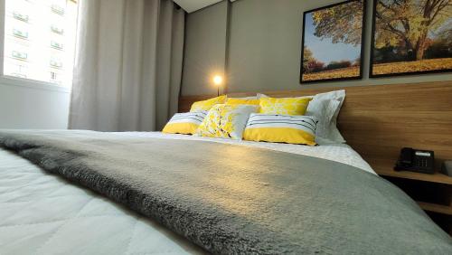 Un dormitorio con una cama grande con almohadas amarillas y blancas en Flat Sunshine - Granja Brasil Resort - Itaipava, en Petrópolis