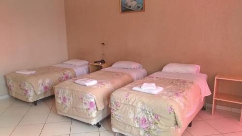 three beds in a room with pink sheets at Hotel Reimann in Indaiatuba