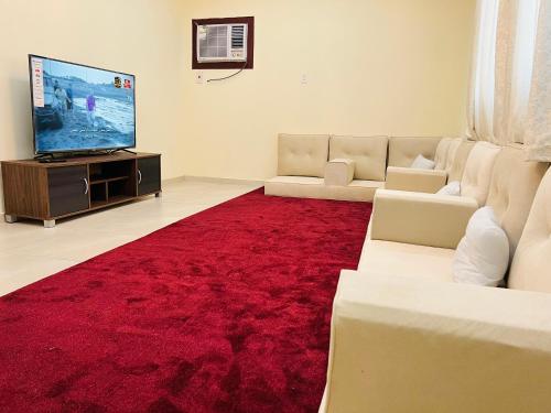 FANATEER SUDAYER VILLA في Al Fanātīr: غرفة معيشة مع سجادة حمراء وتلفزيون بشاشة مسطحة