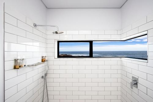 a white bathroom with a view of the ocean at OnTheRocksBB Solar Powered Guesthouse and Ocean Lodge in Bettyʼs Bay