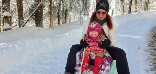 a woman and a child sitting in the snow at nawu apartments & Restaurant in Hermagor