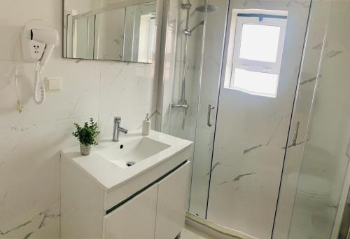 La salle de bains blanche est pourvue d'un lavabo et d'une douche. dans l'établissement CASA MR, à Nazaré