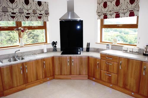 uma cozinha com armários de madeira, um lavatório e 2 janelas em Glendun Self Catering em Cushendall