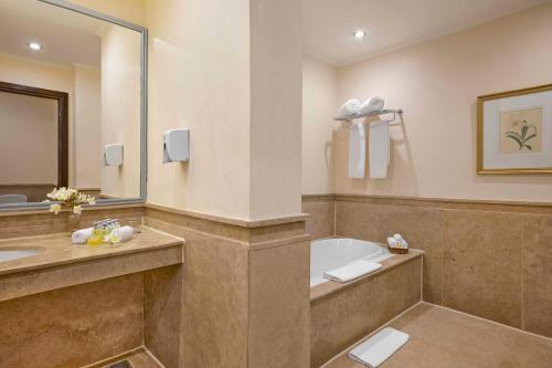 a bathroom with a tub and a sink and a mirror at Jaz Lamaya Resort in Coraya Bay