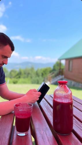 a man sitting on a picnic table with a book and a drink at Ethno village & resort Ćorić in Mojkovac