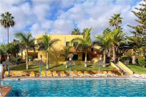 a resort with a swimming pool with chairs and palm trees at Corralejo Garden House in La Oliva