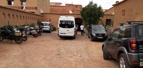 a white bus parked next to a building with parked motorcycles at La Fibule D'or in Aït Ben Haddou