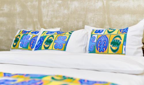 ロメにあるHotel M'Rodeのベッド(白いシーツ、カラフルな枕付)