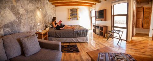 a woman sitting on a bed reading a book in a living room at Lodge Quelana in San Pedro de Atacama